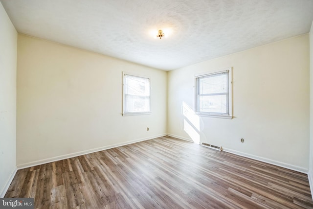 empty room featuring visible vents, a textured ceiling, baseboards, and wood finished floors