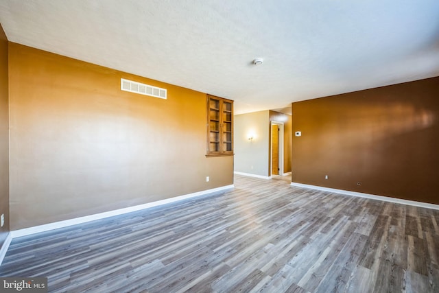 unfurnished room featuring visible vents, a textured ceiling, baseboards, and wood finished floors