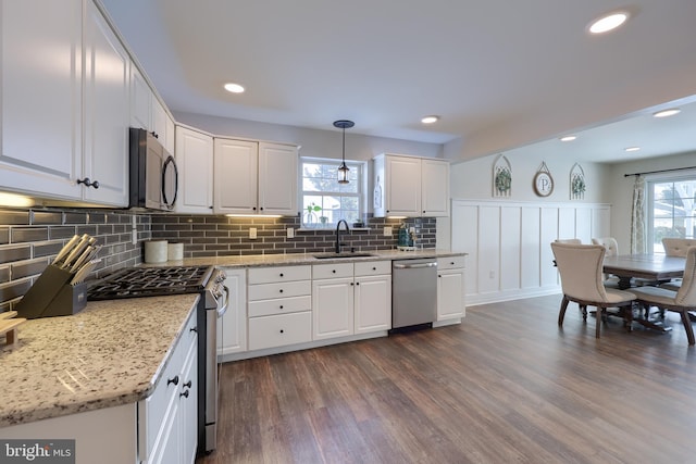 kitchen with sink, appliances with stainless steel finishes, white cabinetry, light stone countertops, and decorative light fixtures