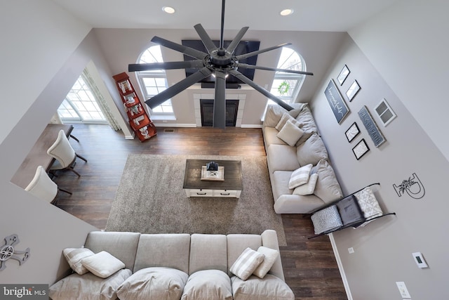 living room with a tile fireplace, a healthy amount of sunlight, dark wood-type flooring, and ceiling fan