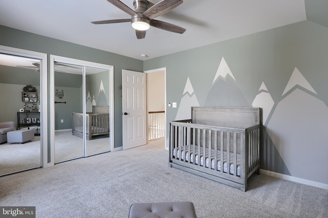 bedroom featuring ceiling fan, a nursery area, carpet flooring, two closets, and vaulted ceiling