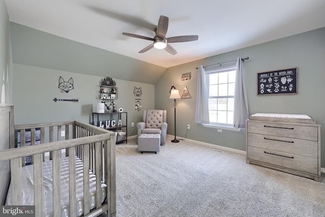 carpeted bedroom featuring a crib, lofted ceiling, and ceiling fan