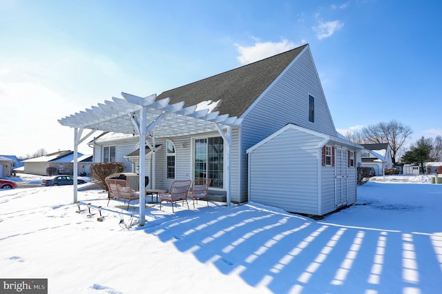 snow covered back of property with a jacuzzi and a pergola