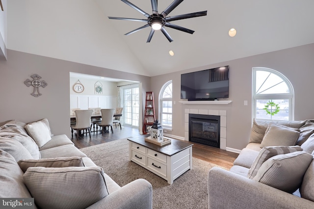 living room featuring a tile fireplace, wood-type flooring, ceiling fan, and high vaulted ceiling