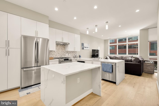 kitchen featuring light stone counters, a center island, appliances with stainless steel finishes, decorative backsplash, and white cabinets