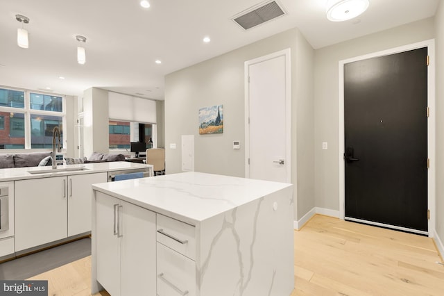 kitchen with sink, white cabinetry, light stone counters, a center island, and light wood-type flooring