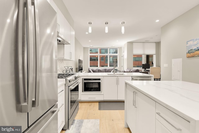 kitchen with appliances with stainless steel finishes, white cabinetry, backsplash, light stone counters, and light hardwood / wood-style floors