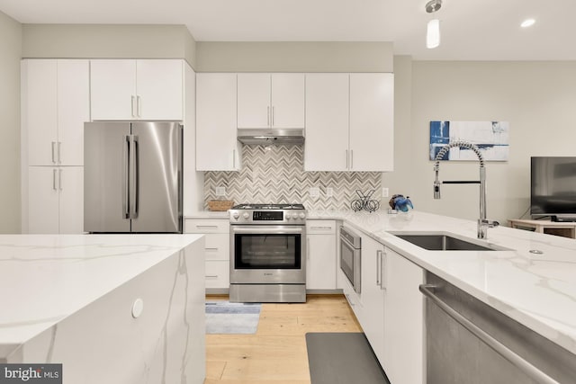 kitchen featuring appliances with stainless steel finishes, tasteful backsplash, white cabinetry, sink, and light stone counters