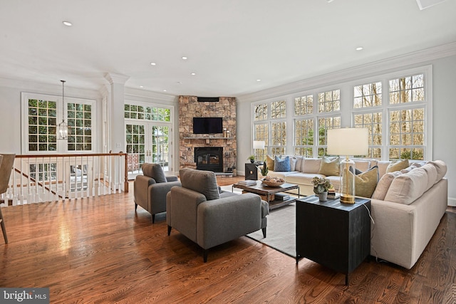 living room with a stone fireplace, dark wood-type flooring, ornamental molding, and a wealth of natural light