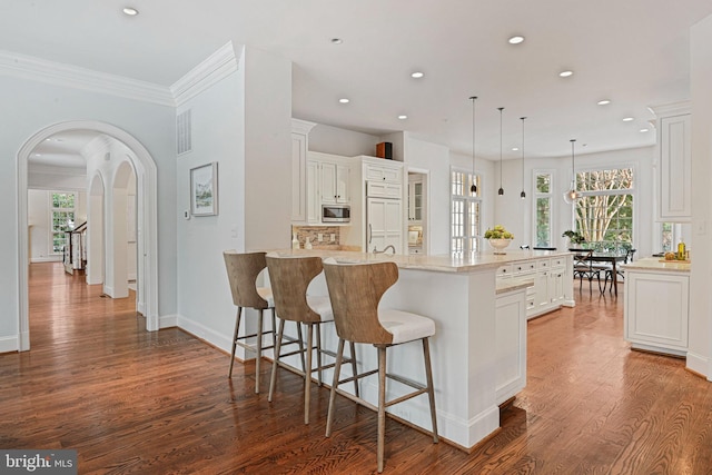 kitchen featuring a large island, built in appliances, hardwood / wood-style flooring, and white cabinets