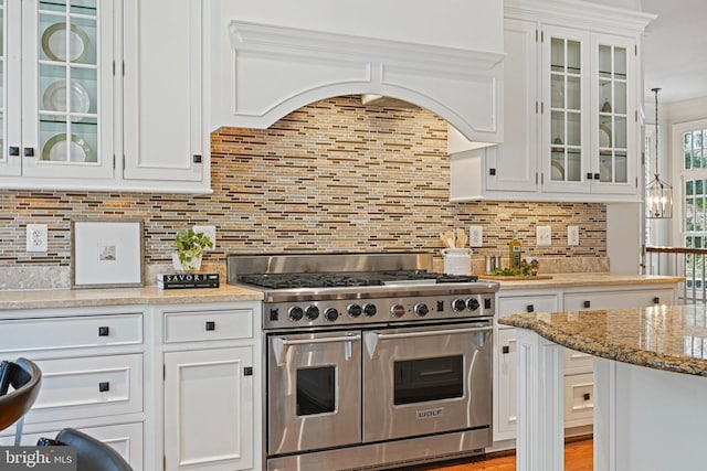 kitchen featuring white cabinetry, backsplash, extractor fan, light stone countertops, and range with two ovens