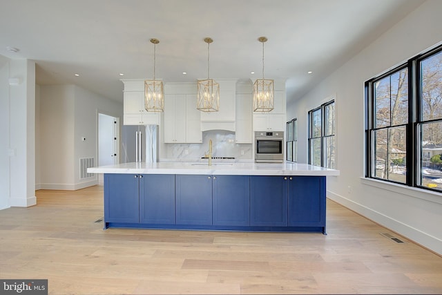 kitchen featuring tasteful backsplash, stainless steel appliances, pendant lighting, white cabinetry, and a large island with sink