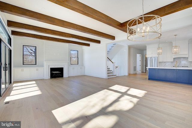 unfurnished living room with beam ceiling, light hardwood / wood-style flooring, sink, and a chandelier