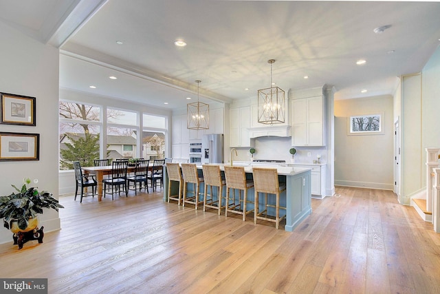 kitchen with stainless steel appliances, white cabinets, decorative light fixtures, light wood-type flooring, and a large island with sink