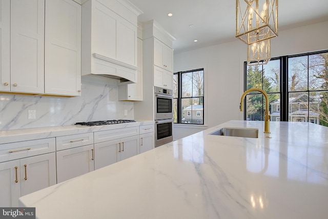 kitchen featuring white cabinetry, sink, light stone countertops, and pendant lighting