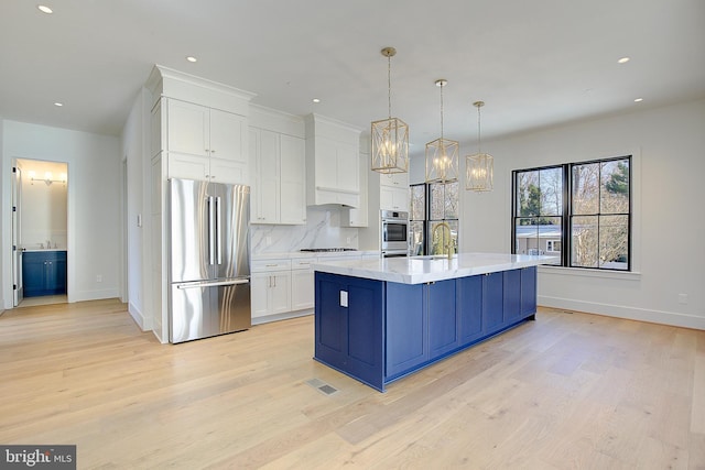 kitchen with stainless steel appliances, pendant lighting, sink, white cabinetry, and a kitchen island with sink