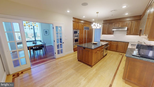 kitchen featuring a kitchen island, tasteful backsplash, dark stone countertops, a notable chandelier, and stainless steel appliances