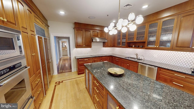 kitchen featuring sink, appliances with stainless steel finishes, decorative backsplash, decorative light fixtures, and dark stone counters