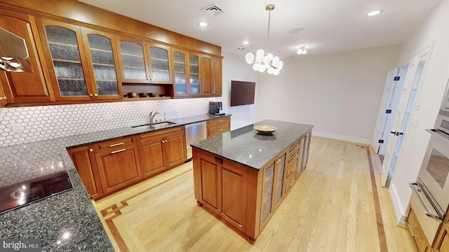 kitchen featuring sink, dishwasher, dark stone countertops, decorative backsplash, and decorative light fixtures