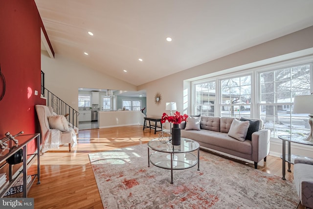 living room with a healthy amount of sunlight, beam ceiling, high vaulted ceiling, and light hardwood / wood-style flooring