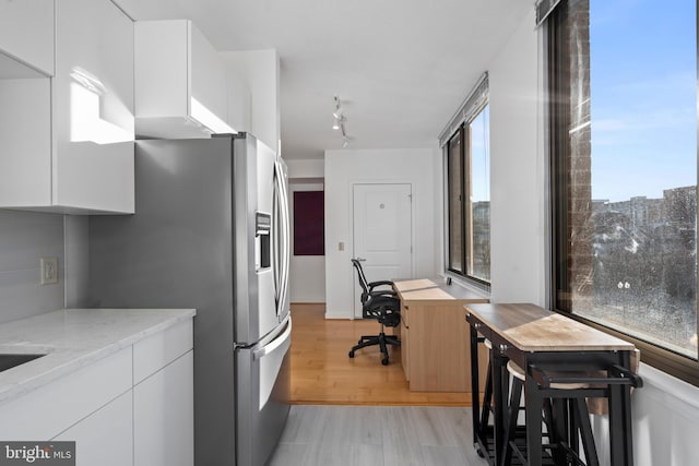 kitchen with light stone counters, stainless steel fridge with ice dispenser, white cabinets, and light wood-type flooring