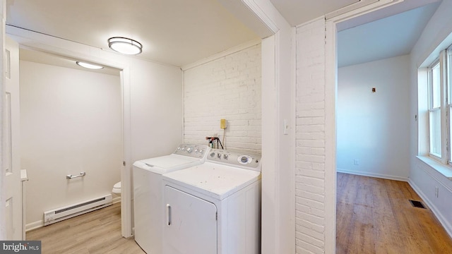 laundry area featuring brick wall, washer and clothes dryer, light wood-type flooring, and a baseboard heating unit