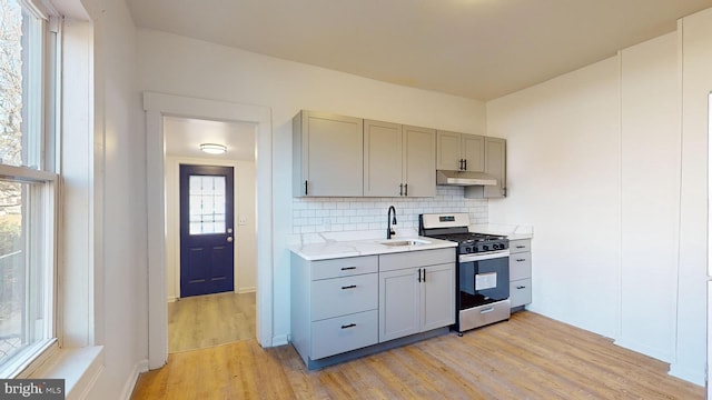 kitchen featuring stainless steel gas range, sink, tasteful backsplash, gray cabinets, and light hardwood / wood-style floors