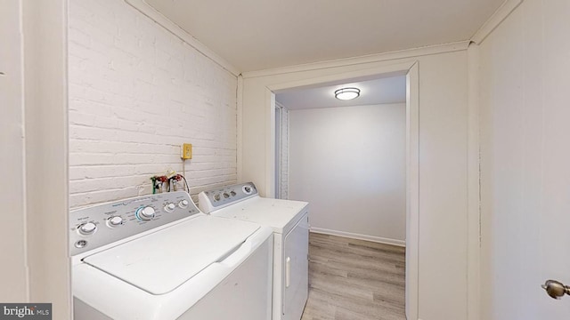 laundry room featuring ornamental molding, brick wall, washer and clothes dryer, and light wood-type flooring