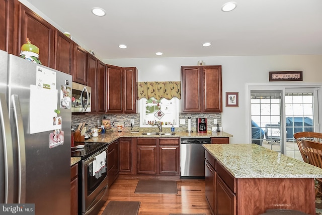 kitchen with a kitchen island, sink, dark hardwood / wood-style flooring, light stone counters, and stainless steel appliances