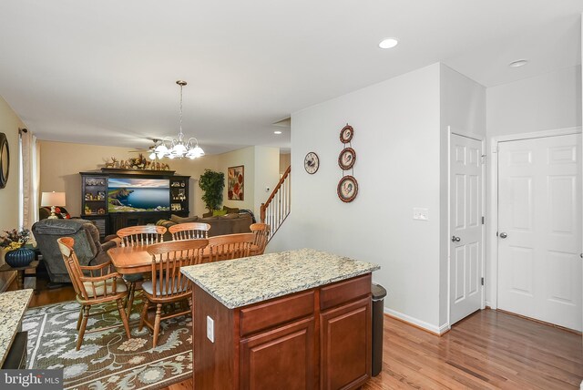 kitchen with a kitchen island, hanging light fixtures, light stone counters, light hardwood / wood-style floors, and an inviting chandelier