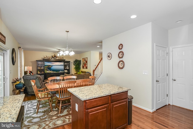 kitchen with a kitchen island, hanging light fixtures, light stone countertops, an inviting chandelier, and light hardwood / wood-style flooring