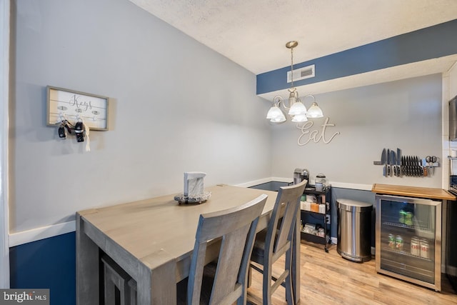 dining room featuring a textured ceiling, beverage cooler, a chandelier, and light wood-type flooring