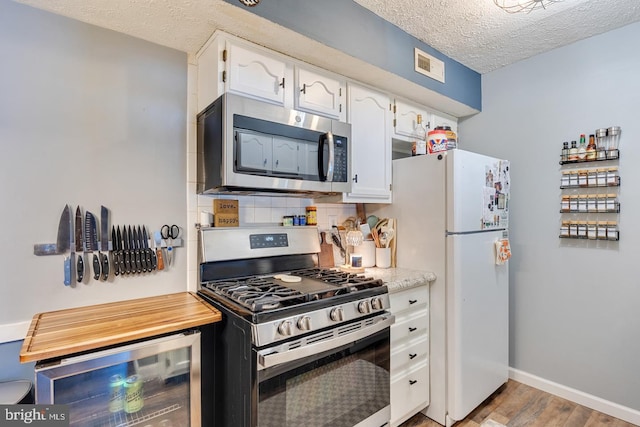 kitchen featuring stainless steel appliances, wine cooler, light hardwood / wood-style floors, a textured ceiling, and white cabinets