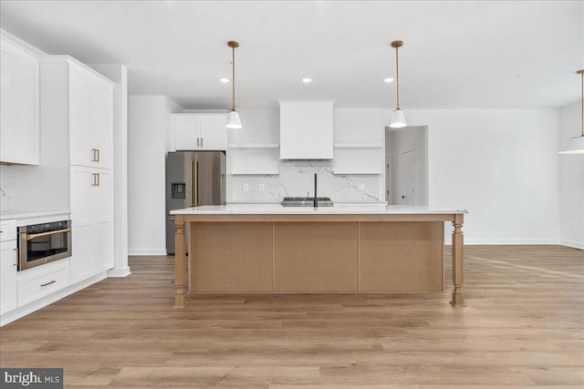 kitchen with decorative light fixtures, stainless steel appliances, an island with sink, and white cabinets