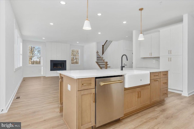 kitchen featuring pendant lighting, sink, dishwasher, white cabinetry, and an island with sink