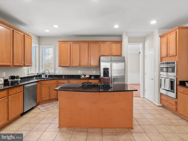 kitchen with sink, light tile patterned floors, appliances with stainless steel finishes, a center island, and dark stone counters