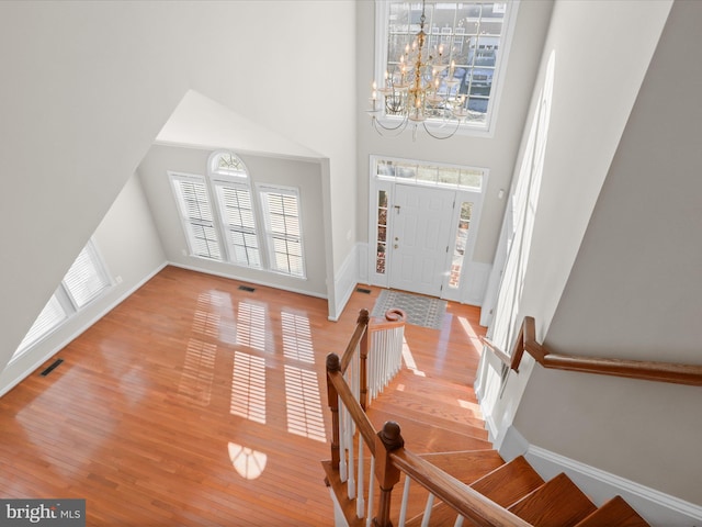 foyer entrance featuring hardwood / wood-style flooring, a towering ceiling, and a chandelier