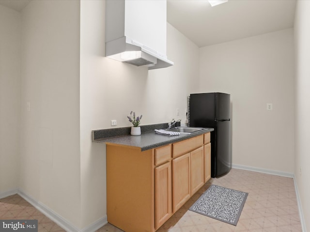 kitchen featuring black refrigerator, sink, and wall chimney range hood