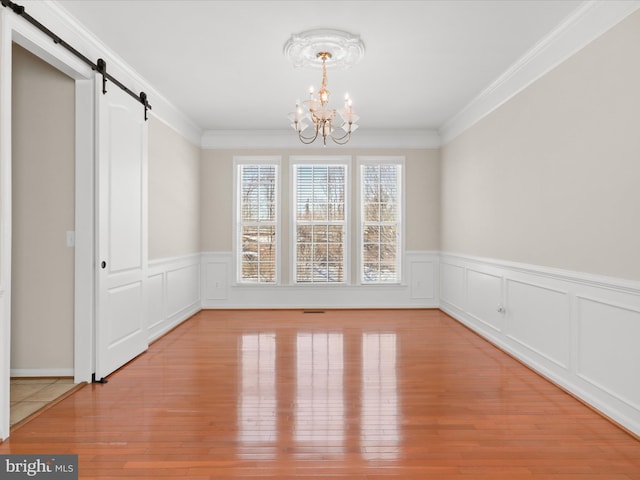 unfurnished dining area featuring crown molding, a barn door, light wood-type flooring, and a notable chandelier