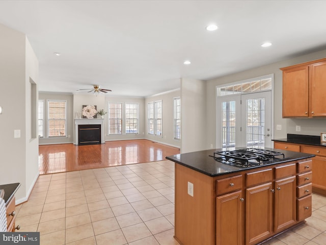 kitchen with light tile patterned flooring, stainless steel gas stovetop, dark stone counters, a center island, and ceiling fan