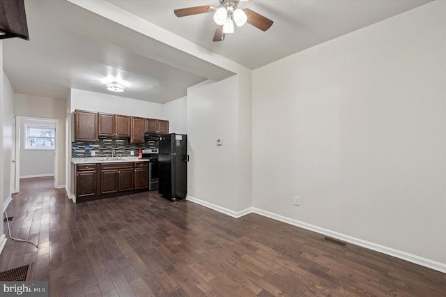 kitchen featuring sink, ceiling fan, black fridge, dark hardwood / wood-style flooring, and decorative backsplash