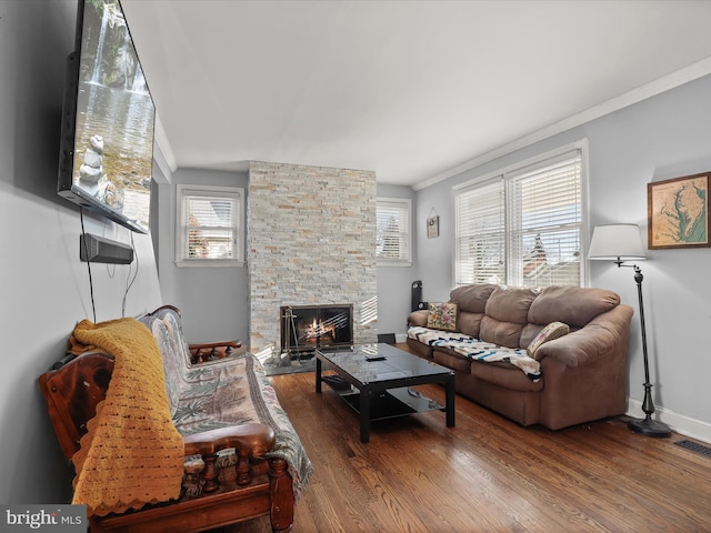 living room featuring a stone fireplace, wood-type flooring, and ornamental molding