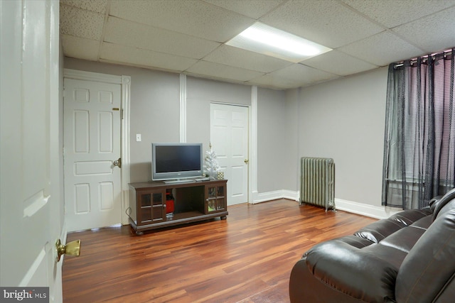 living room featuring dark hardwood / wood-style flooring, radiator heating unit, and a paneled ceiling