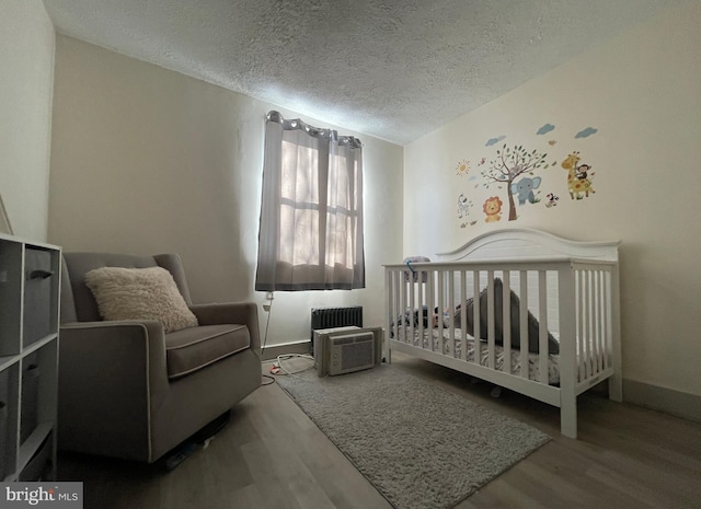 bedroom featuring a nursery area, wood-type flooring, radiator, and a textured ceiling