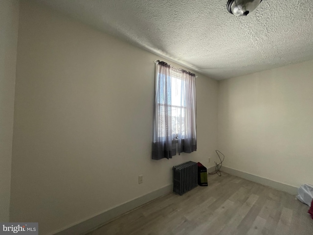 unfurnished room featuring radiator, light hardwood / wood-style flooring, and a textured ceiling