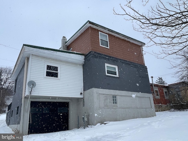 snow covered rear of property featuring a garage