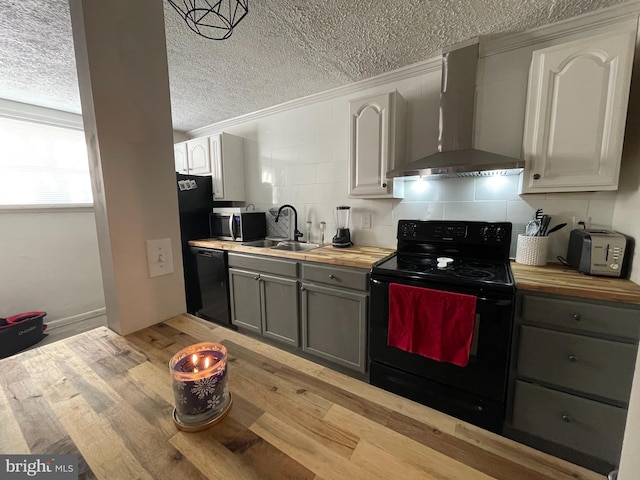 kitchen featuring wall chimney range hood, gray cabinets, butcher block countertops, and black appliances