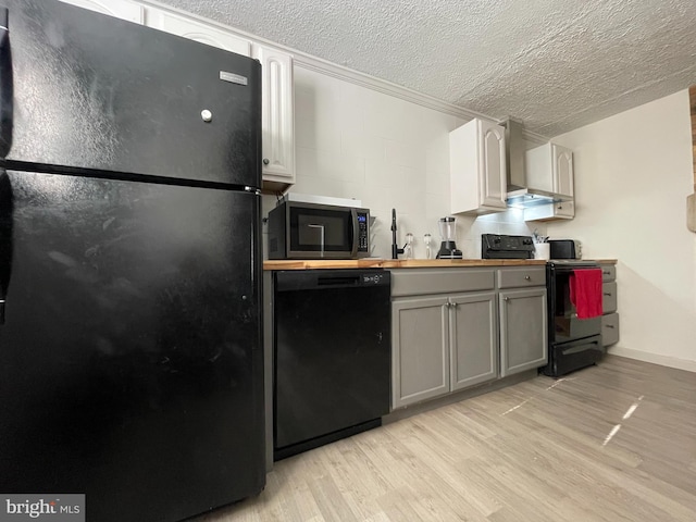 kitchen with wall chimney range hood, gray cabinets, wooden counters, black appliances, and light hardwood / wood-style floors