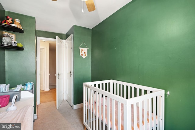 carpeted bedroom with a crib and ceiling fan