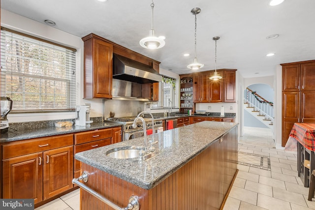 kitchen featuring hanging light fixtures, exhaust hood, a center island with sink, and dark stone counters